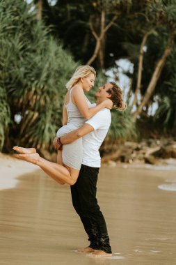 Sahilde kucaklaşan, gülümseyen güzel bir çift. Sevgililer Günü tatilde. Sahilde bir çift. Bir adam bir kızı kollarında tutuyor..