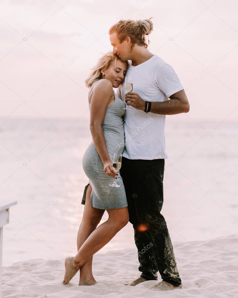 Happy couple drink wine on the beach. Couple in love on sunset background. Valentines day in vacation. Travel, love, youth lifestyle concept. Look into the eyes close up view couple drinking vine on sunset