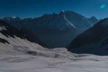 Dramatic view after sunrise during camping and trekking amongst the snow covered Swargarohini mountains under a clear blue sky in the Sankri region of Uttarakhand state, Indian Himalayas.