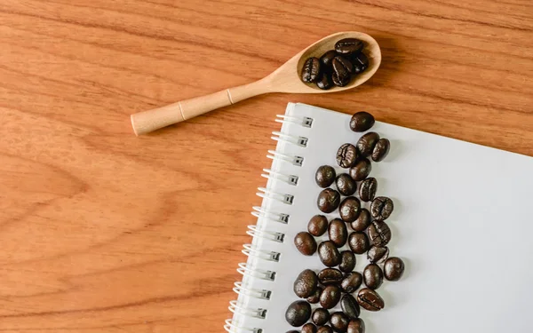 Kaffeebohnen mit Holzlöffel und Notizbuch auf Holztisch. — Stockfoto