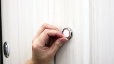 Bir kadının eli, kapı deliğinin kapağını sorunsuzca açar. Yakın plan. Paranoya ve röntgencilik kavramı..