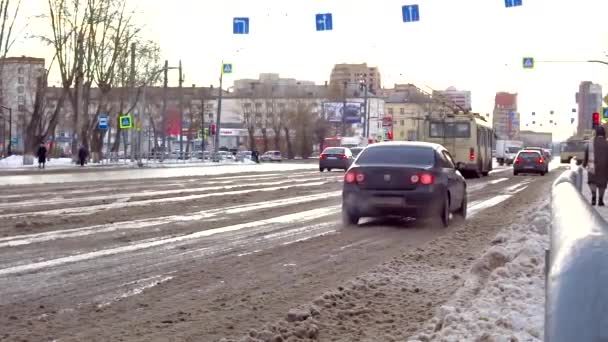 La chaussée, les voitures roulent sur la neige mouillée, éclaboussant la boue. Arrêts de transport à un feu rouge devant l'intersection. — Video