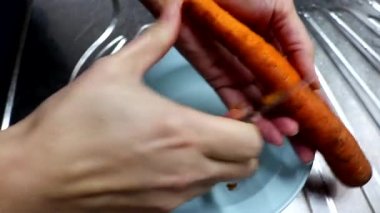 Bir kadın olgun bir havucu bıçakla soyar. Mutfakta yemek pişirmek..