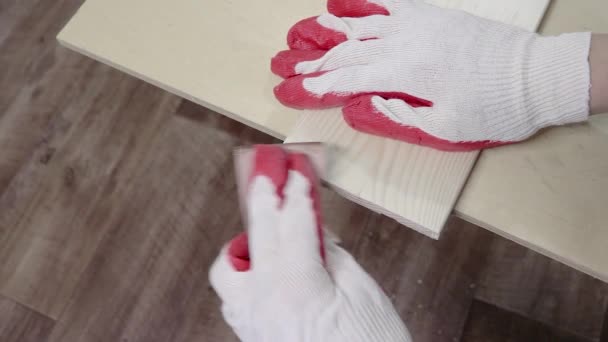 Lijar los bordes de tablones de madera de pino con papel de lija. Las manos en los guantes de trabajo procesan madera, carpintería. — Vídeos de Stock