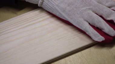 İş eldivenindeki bir el ahşap bir kalası okşar - pürüzsüzlük için tahtanın kalitesini kontrol eder. Marangozluk işi.