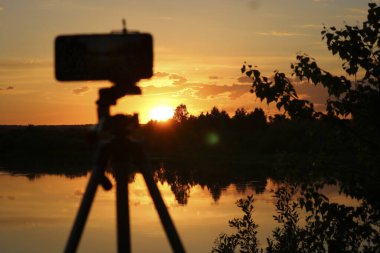 Nehrin üzerinde renkli bir günbatımının akıllı telefonuyla hızlandırılmış bir video çekmek. Seçici odak.
