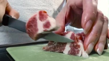 Bir kadın büyük bir parça domuz etini bıçakla kesiyor. Yağ tabakalı et, domuz boynu..