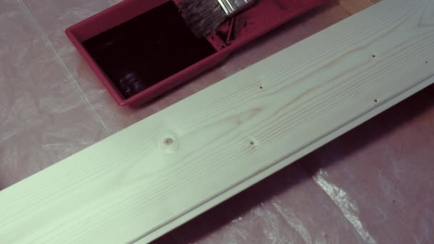 Un travailleur ganté peint une planche de pin clair avec une tache foncée avec une brosse sur la deuxième couche. Travaux de peinture. — Video