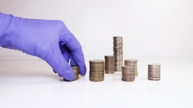 Tıbbi eldivendeki bir el, madeni paraları bir sütuna koyar. Yatırım konsepti. Metalik para birimi. Hijyene uyum.