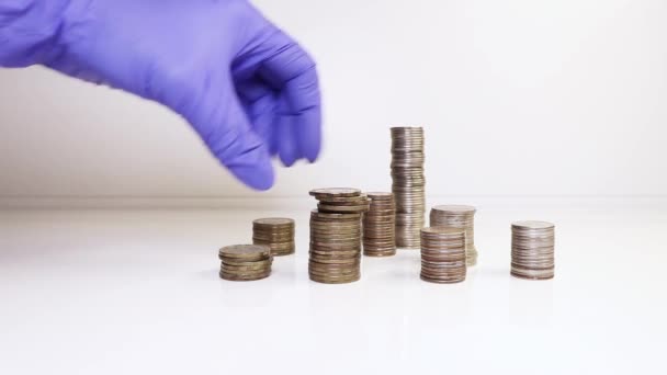Eine Hand in medizinischen Handschuhen legt Münzen in eine Säule. Investitionskonzept. Metallische Währung. Einhaltung der Hygiene. — Stockvideo