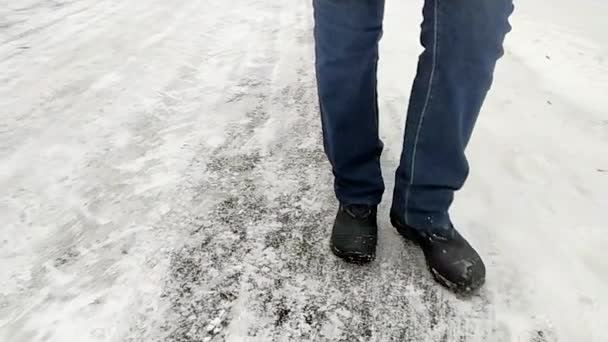 Benen på en person i vinterkängor och jeans går på den snötäckta asfalten. Vintervandring koncept. Låg sikt, slowmotion 240 fps. — Stockvideo