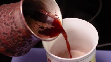 Sıcak demlenmiş doğal kahve bir Türk 'ten bir fincan süte dökülür. Lezzetli bir sıcak içecek pişiriyorum. Seçici odaklanma. Bulanık video.