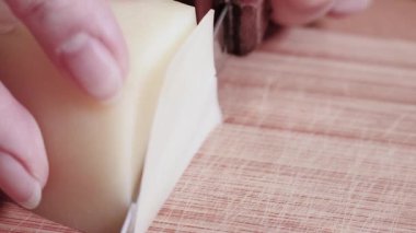 Sert basılmış keçi peyniri tahta kesme tahtasının ince dilimlerine ayrılır. Avrupa kahvaltısı hazırlıyorum. Kadın eli, peyniri bıçakla kesti. Seçici odak.