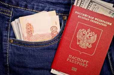 A stack of American hundred dollar bills in the international passport of Russia and Russian rubles in a pocket of blue jeans. Money, cash. Travel concept.