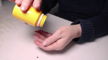 Yaşlı bir kadın şişeden eline ilaç döküyor. Kırışıklıkları olan eller. Sağlığın korunması ve yaşlılara bakılması..