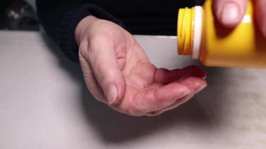 Yaşlı bir kadın şişeden eline ilaç döküyor. Kırışıklıkları olan eller. Sağlığın korunması ve yaşlılara bakılması..