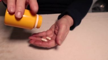 Yaşlı bir kadın şişeden eline ilaç döküyor. Kırışıklıkları olan eller. Sağlığın korunması ve yaşlıların bakımının sağlanması. Sepia tonlu video