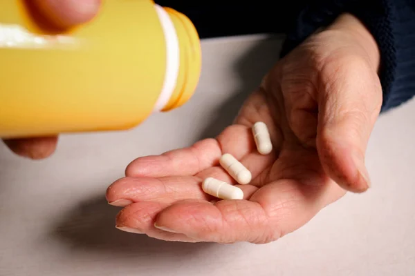 An elderly woman pours pills from a jar into her hand. Elderly health concept. Nursing and caring for elderly parents. Selective focus.