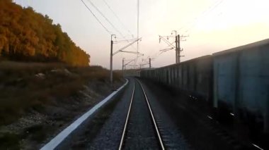 Gün batımında trenin son vagonunun penceresinden bak, raylar uzaklaşıyor. Yük treni yaklaşan raylarda ilerliyor. Tren yolculuğu kavramı.