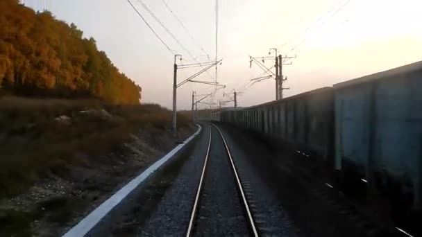 Vista da janela da última carruagem do trem ao pôr do sol, trilhos indo para a distância. O trem de carga está viajando em trilhos próximos. Conceito viagem de trem. — Vídeo de Stock