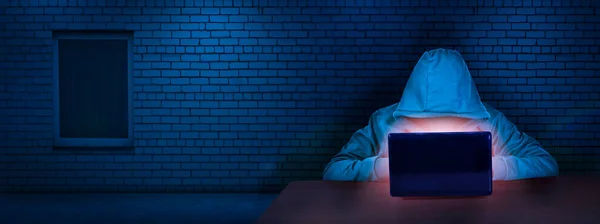 Hacker, tuğladan duvarı olan bir odada dizüstü bilgisayar ekranının arkasında çalışıyor. İnternet suçları. Hackleme ve kötü amaçlı yazılım konsepti, siber güvenlik. Dijital suçlar.