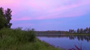 Gölün üzerinde gün batımı. Batan güneşin aydınlattığı pembe bulutlar. Doğanın sakinliği ve sakinliği.