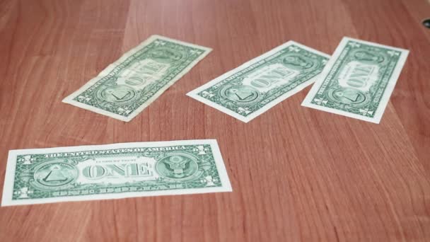 Billetes americanos de un dólar y cien dólares están volando sobre una mesa de madera. Entonces las manos de las mujeres los recogen en una pila. — Vídeos de Stock