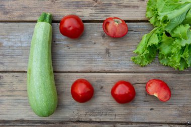 Tahta bir masada domates, kabak ve yeşil marul yaprakları.