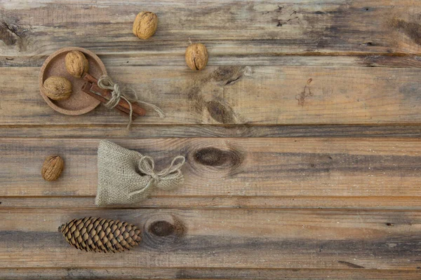 Nueces, una bolsa, canela y un cono de abeto en el fondo de viejas tablas de madera. — Foto de Stock