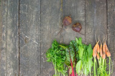 Genç havuç, taze pancar yaprağı ve eski ahşap bir masanın yüzeyinde kuş sürüsü.