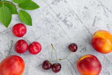 Taze erik, şeftali ve kiraz. Masanın üzerinde yapraklar var. Boşluğu kopyala
