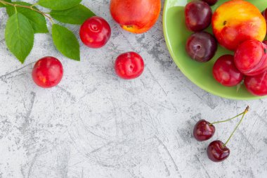 Taze erik, şeftali ve kiraz. Masanın üzerinde yapraklar var. Boşluğu kopyala