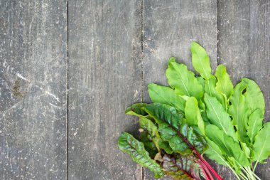 Eski ahşap bir masanın yüzeyinde taze pancar kökü ve at yaprakları.