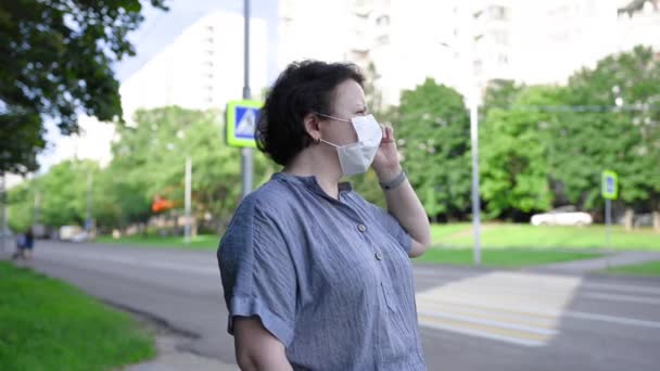 En kvinna i medicinsk mask på gatan i stan. Video med en statisk kamera. — Stockvideo