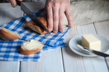 Geleneksel kahvaltı yemekleri. Adamın elleri masanın üzerinde ekmek ve peçeteyle ekmek kesti. Yakın çekim.