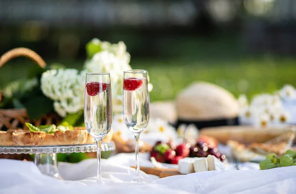 Summer picnic in the Park with champagne. Celebration. Fresh fruit and delicious pastries, cheese and sausage, a hat and a basket of flowers