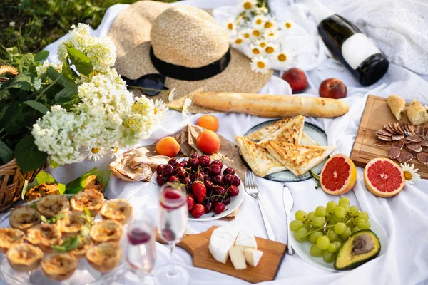 Summer picnic in the Park with champagne. Celebration. Fresh fruit and delicious pastries, cheese and sausage, a hat and a basket of flowers