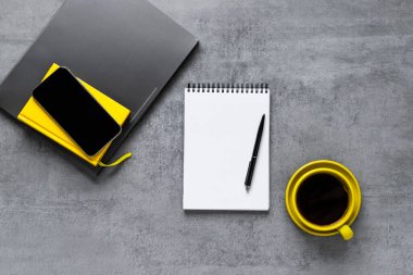 Gri beton bir masada dizüstü bilgisayar, telefon ve ofis malzemeleri. Sarı bardakta kahve. İş yeri. Çalışma masası. Uzaktan kumanda. Mesafe öğrenme. sarımsı ve aşırı gri. 2021 'in rengi. Boşluğu kopyala