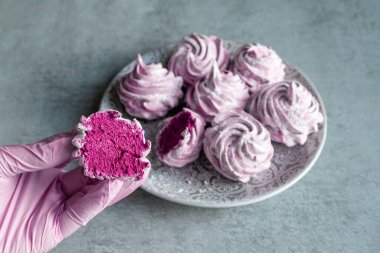 Leylak eldivenli bir kadının elinde ev yapımı bir lokum var. Gri arkaplan