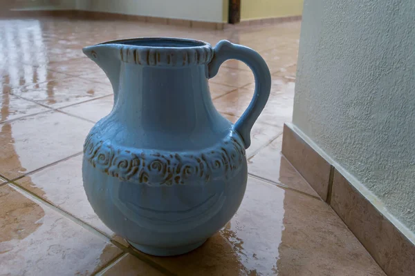 jug on the floor. ceramic blue jug for collecting water in a damp room during the rain. wet tile floor, water drops on a beautiful jug with ornaments. rainy season in thailand