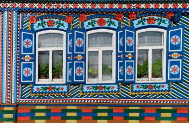 Bir kır evinin camları buğulanmış. Kesik çiçeklerle oyulmuş kepenkler ve pencerelerde çeşitli desenler. Parlak renkler kullanılır. Geleneksel Rus tarzı. Kunara (Rusya)
