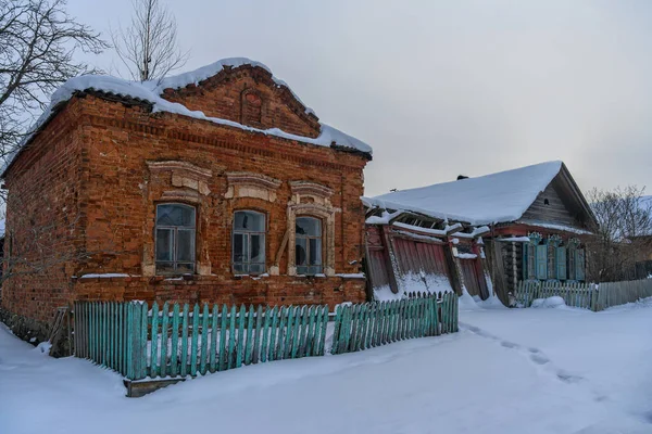 old brick house in the historic village of Byngi (Nevyanskiy district, Russia) in winter. close-up. antique shaped brickwork of walls. wooden blue fence. frosty winter day with white snow