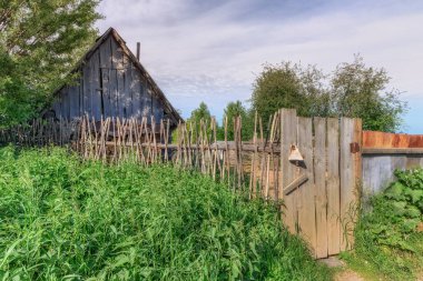 Eski ahşap ev. Ahşap çitleri, kapısı ve kış için yakacak odunu olan ahşap bir ev. Evin girişinde uzun ısırgan otları yetişti. Köyde yaz bulutlu bir gün