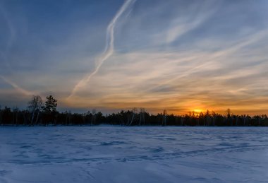 Bir kış sabahı, ormanın yakınındaki donmuş bir gölün üzerinde gün doğumu. Güneşin doğuşuyla güzel turuncu-mavi gökyüzü. Karlı bir gölün dalgalı yüzeyi. Kış ormanında yürüyüş.