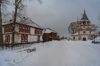 Kış manzarası görkemli eski bir kilise, tarihi vali evi, karda bir bank ve uzun ağaçlar. Kış bulutlu bir günde Solikamsk (Kuzey Ural, Rusya) şehrinin merkezi 