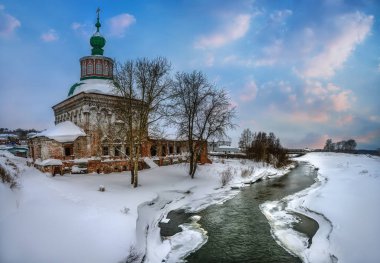 Eski Ural şehri Solikamsk 'taki (Rusya) Usolka Nehri kıyısındaki eski ve restore edilmemiş taş kilisenin soğuk bir kış akşamında manzarası. Uzun ıhlamur ağaçları, bembeyaz kar ve güzel bir gün batımı gökyüzü.