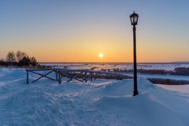 Güneşli bir kış akşamında yüksek dağlık bir kıyıdan Rusya 'nın Sibirya Irmağı vadisine (Sibirya) bakın. Ahşap bir merdiven nehre iniyor, orada bir açık fener var. Çok soğuk. 