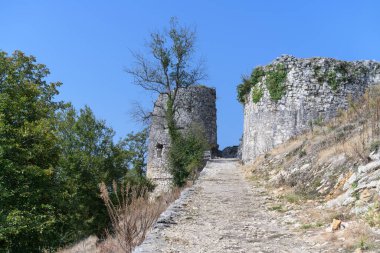 Güneşli bir yaz gününde tarihi bir patika ile Anakopia kalesinin (Yeni Athos, Abhazya) eski harap olmuş savunma kuduzları. Eski taş duvarlar yeşil bitki örtüsüyle kaplı. Bir sürü meşe ağacı
