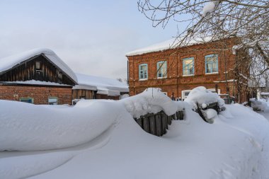 Cherdyn kış eskizleri (Ural, Rusya). Eski kasabadaki eski tuğladan evler, güzel desenli duvarlar. Yüksek kar yığınları nedeniyle ahşap çit neredeyse görünmezdir. Cherdyn 'de dondurucu ve güneşli bir gün 