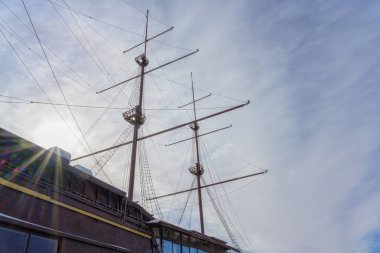 Geminin direkleri mavi ve beyaz gökyüzünün arka planına karşı. Yakın plan. Gemi arka planda vuruldu. Geminin direğinden gökkuşağı ışınları süzülüyor.. 